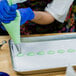 A person in a blue glove using an Ateco plain piping tip to make green pastry.