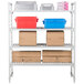 A white Cambro Camshelving® Premium unit with 4 vented shelves holding brown boxes and red and blue containers.