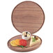 A Cal-Mil wooden round serving board with food including cheese, olives, and yellow and red vegetables.