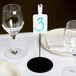 A table with a white Cal-Mil write-on paddle sign next to a plate and wine glass.