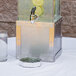 A stainless steel Cal-Mil infusion beverage dispenser with a glass of water and limes in it.