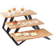 A wooden table with three Cal-Mil bamboo stair-step risers holding food.