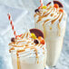 Two glasses of milkshakes with whipped cream and caramel toppings made with REESE'S Peanut Butter Sauce on a table.