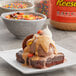 A brownie with ice cream, chocolate sauce, and a jar of REESE'S Peanut Butter Sauce on a table.