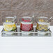 A Cal-Mil stainless steel display with 3 notched glass jars of lemons, limes, and green olives.
