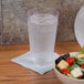 A bowl of salad with lettuce, tomatoes, and croutons next to a GET Customizable plastic pint glass filled with water.