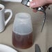 A hand using a Tablecraft polypropylene dispenser to pour brown liquid into a small container.