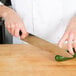 A person using a Victorinox Chef Knife to slice a cucumber on a wooden surface.