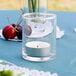A candle in a Libbey glass votive holder on a table.