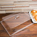 A clear Cal-Mil rectangular tray cover on a wood surface with a plate of bagels inside.