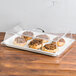 A clear plastic rectangular tray cover over a table of pastries.