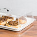 A Cal-Mil rectangular clear tray cover on a table in a bakery display with pastries inside.
