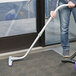 A person using a ProTeam telescoping wand to vacuum a carpeted floor.