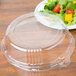 A clear plastic WNA Comet lid on a table next to a plate of salad.