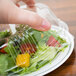 A hand putting a salad in a WNA Comet plastic container with a lid.