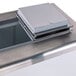 A rectangular stainless steel box with a square opening on a metal surface.