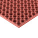 A close up of a large red circular Notrax rubber mat with small holes.