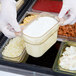 A person in white gloves holding a Cambro plastic food container filled with food.
