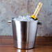 A stainless steel American Metalcraft double wall champagne bucket holding a bottle of champagne on a table with ice.