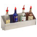 A stainless steel Advance Tabco speed rail holding three bottles of liquor on a counter.