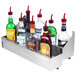 A stainless steel Advance Tabco double tier speed rail on a counter holding several bottles of alcohol.