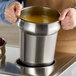 A person holding a 4 qt. stainless steel inset with soup in it.