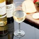 A Libbey white wine glass filled with white wine next to a cheese and fruit platter.