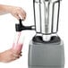 A person pouring a pink liquid into a Waring stainless steel blender jar.