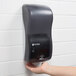 A hand using a black San Jamar touchless soap dispenser.