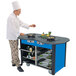 A chef cooking on a stainless steel induction cooking cart with a royal blue laminate finish.