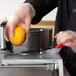 A person using the Vollrath 1/4" InstaSlice pusher head to cut an orange.