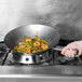 A hand cooking shrimp and vegetables in a Vollrath carbon steel wok on a stove.