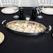 A bowl of food in a Vollrath Miramar oval au gratin dish on a table.