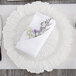 A white napkin with purple flowers on a Charge It by Jay Reef white charger plate.