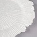 A white Charge It by Jay glass charger plate with a large shell pattern.