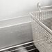 A Pitco stainless steel floor fryer with a basket and metal bar inside.