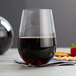 A Stolzle stemless wine glass filled with red wine next to crackers and strawberries.