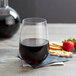 A Stolzle stemless wine glass filled with red wine next to a plate of crackers and strawberries.