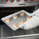 A gloved hand holding a Chicago Metallic rimmed sheet pan with cinnamon rolls.