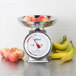 An Edlund stainless steel portion scale on a counter with apples and bananas in a bowl.