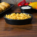 A Hall China black oval baker dish filled with macaroni and cheese on a table.