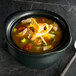 A black Hall China onion soup bowl filled with chicken and vegetables.