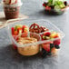 A Fabri-Kal Greenware 3-compartment plastic container with fruit, nuts, and pretzels in it.