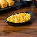A black Hall China rarebit dish filled with macaroni and cheese on a table set with breadsticks and carrots.