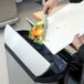 A hand using a knife to cut vegetables into a Rubbermaid Slim Jim trash can.
