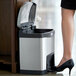 A woman in high heels stepping into a Rubbermaid Slim Jim stainless steel rectangular front step-on trash can.