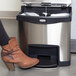 A person using a Rubbermaid Slim Jim front step-on trash can with a brown boot.