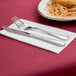 A napkin with a fork and knife next to a plate of spaghetti.