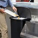 A man using a Rubbermaid Slim Jim front step-on trash can to throw away a lemon slice.