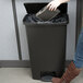 A woman using a Rubbermaid Slim Jim black step-on trash can.